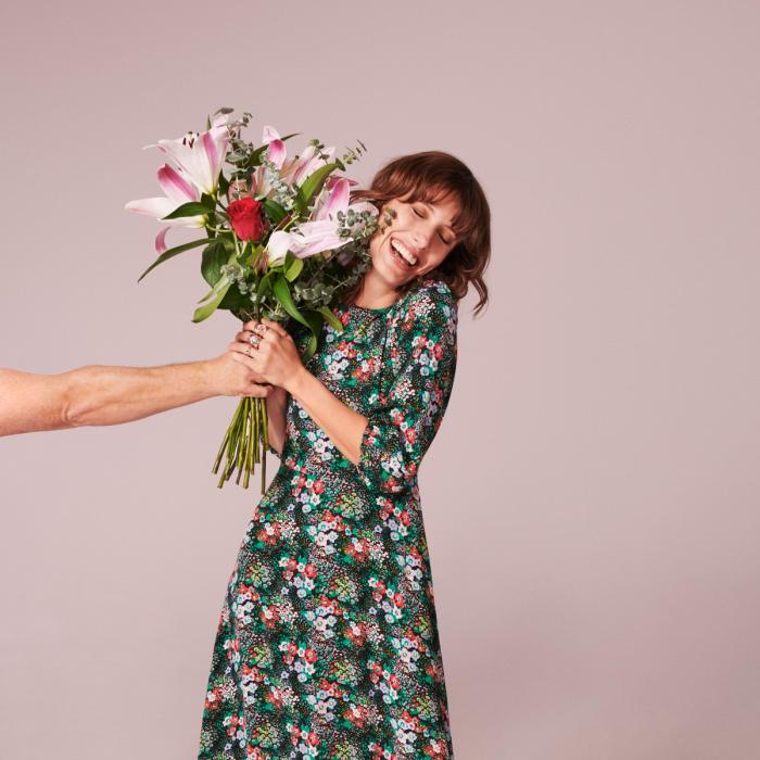 Woman in long floral dress being given a bouquet of pink flowers