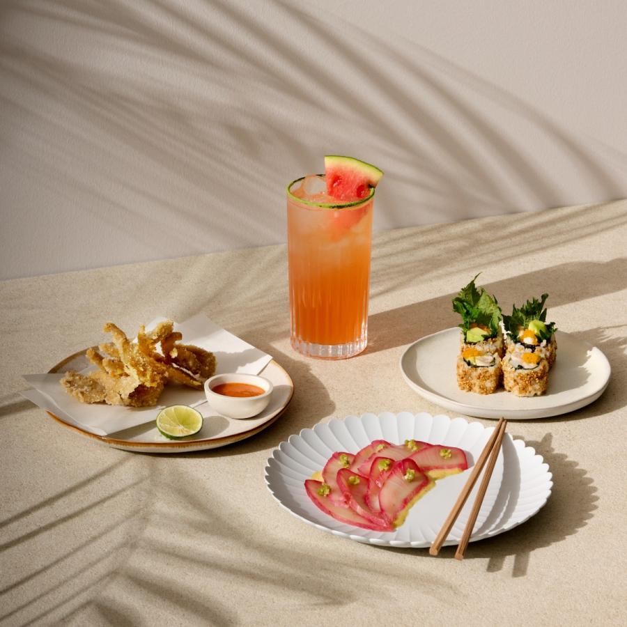 Selection of sushi dishes and a cocktail on a sunlit wooden surface